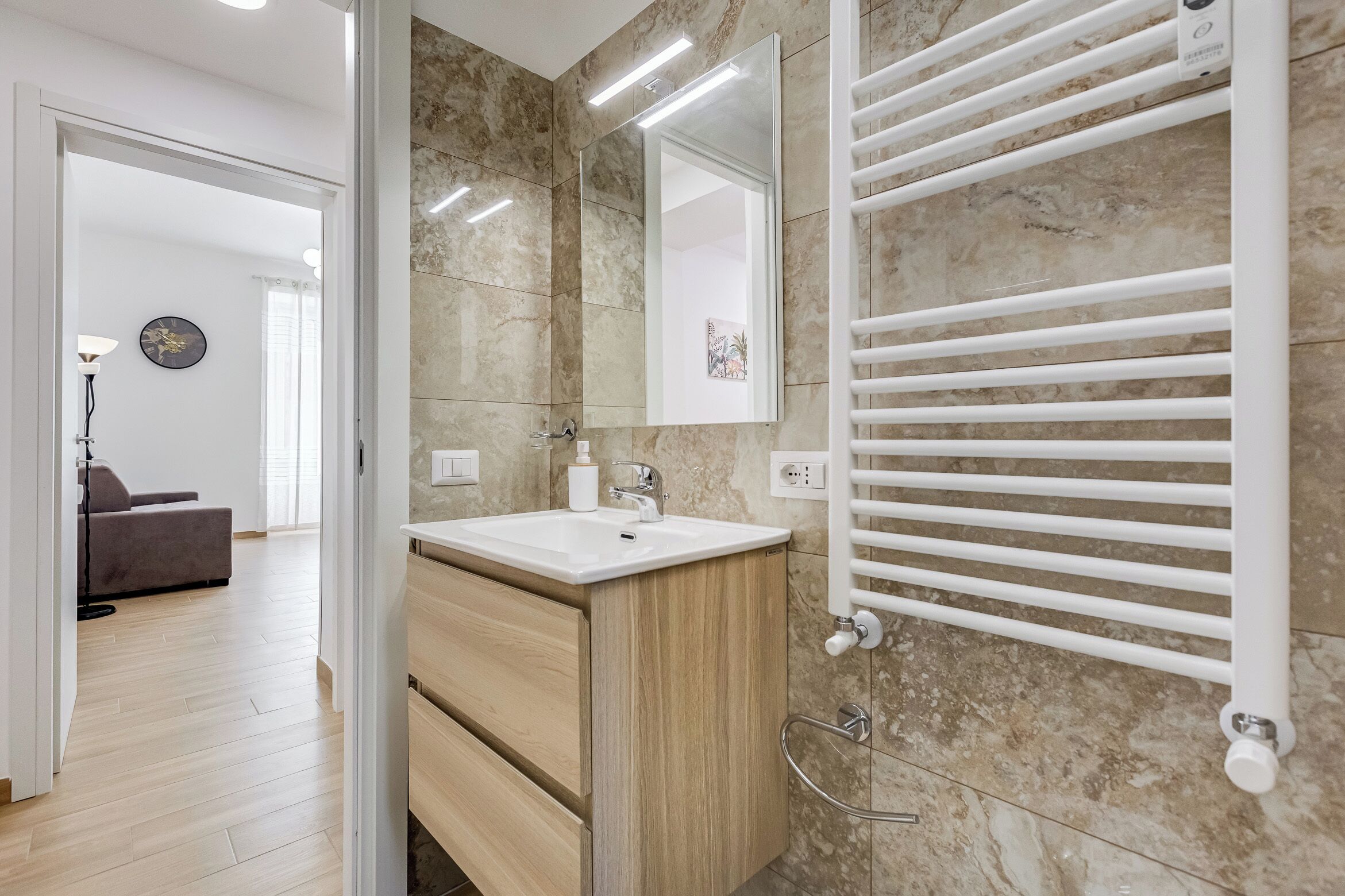 A modern bathroom with a marble-tiled wall, a white sink, and a built-in towel rack.