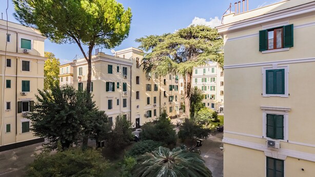 A courtyard with multiple buildings, trees, and a palm tree. - Testaccio Patty Flat (Rome)