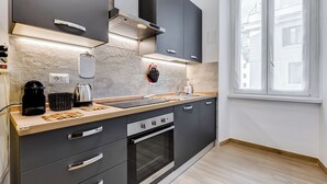 A modern kitchen with dark cabinets, a wooden countertop, a built-in oven, and a window providing natural light. - Testaccio Patty Flat (Rome)