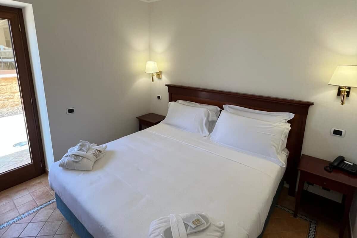Une chambre d’hôtel avec un grand lit, deux tables de chevet, une petite table et une porte donnant sur un balcon.