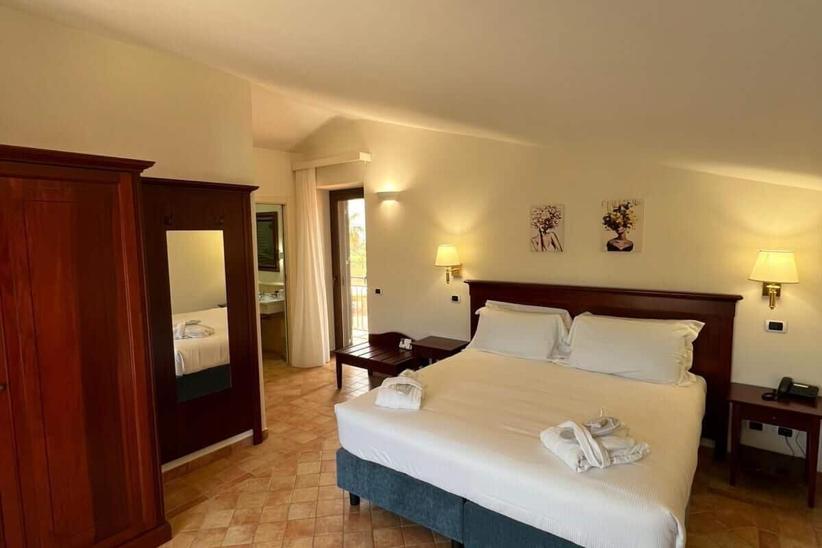 Une chambre d’hôtel avec un lit, un bureau, une chaise, une armoire et une salle de bain visible à travers une porte ouverte.