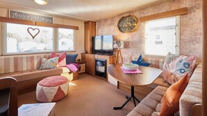 A cozy RV interior with a sofa, ottoman, TV, and a clock on the wall. - Host & Stay | Cosy Cove (Cresswell)