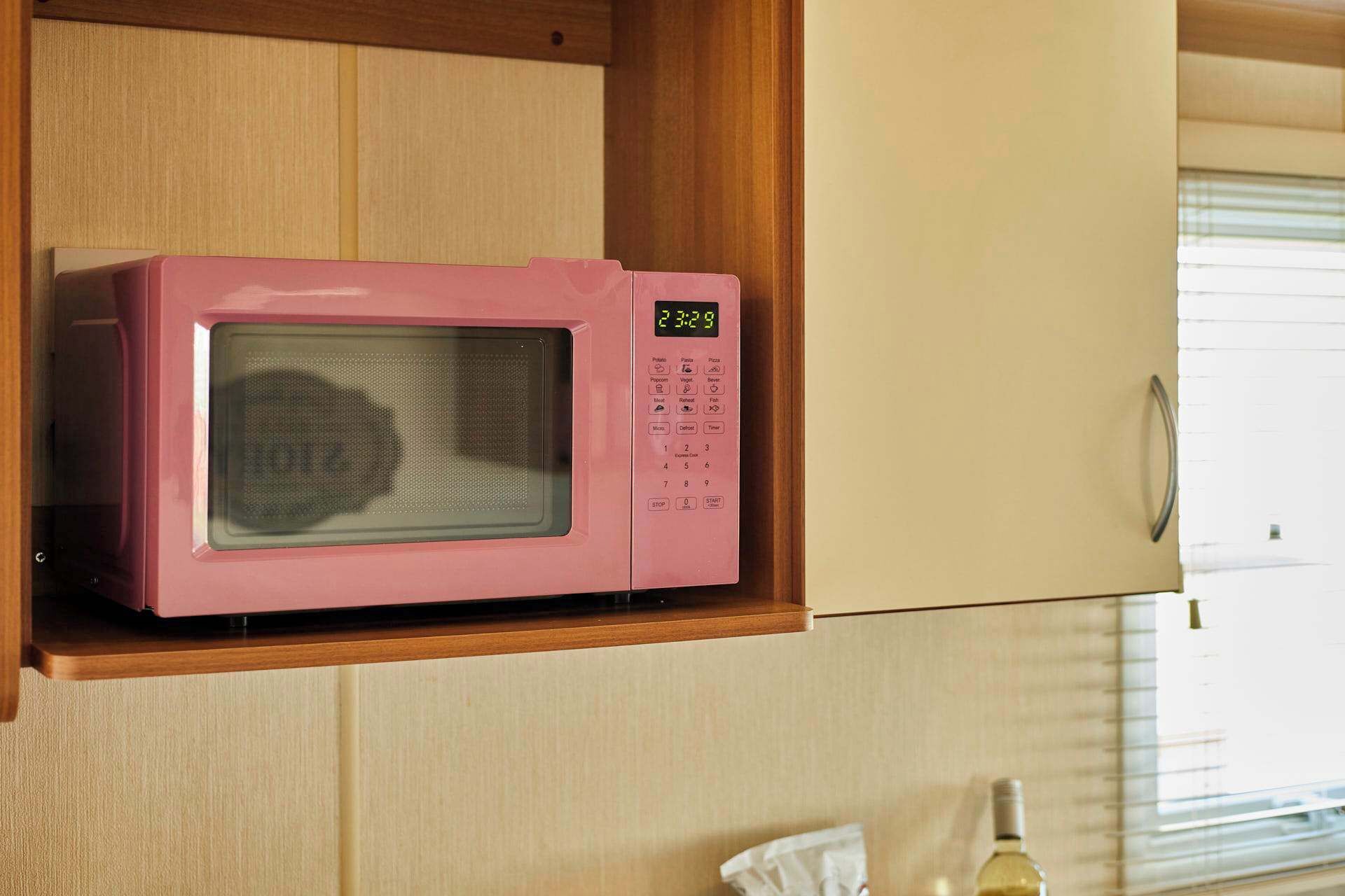 Eine rosa Mikrowelle auf einem Holzboden in einer Küche mit einem Fenster.