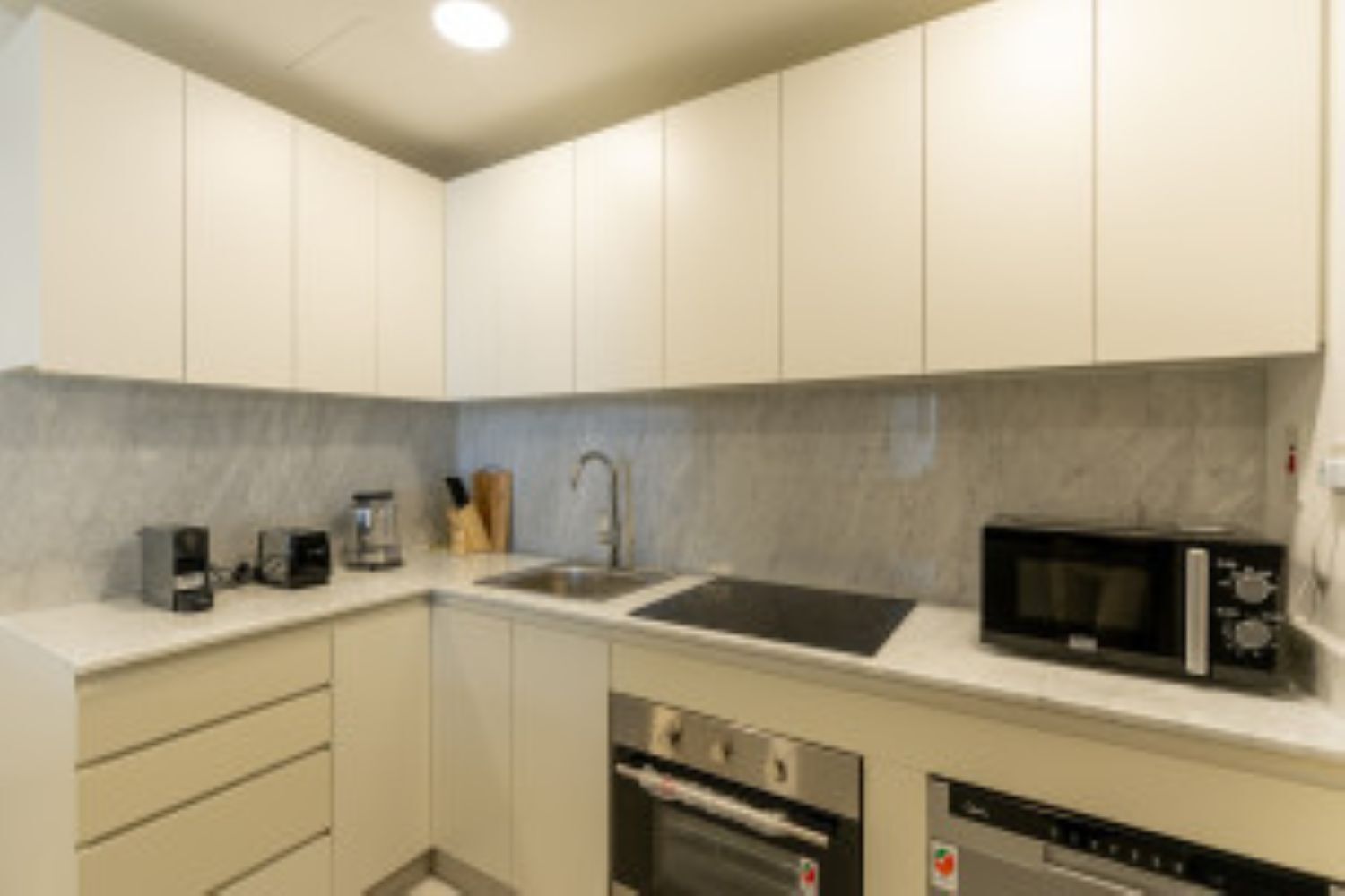 A compact kitchen with white cabinets, a stainless steel sink, a microwave, a coffee maker, and a dishwasher.