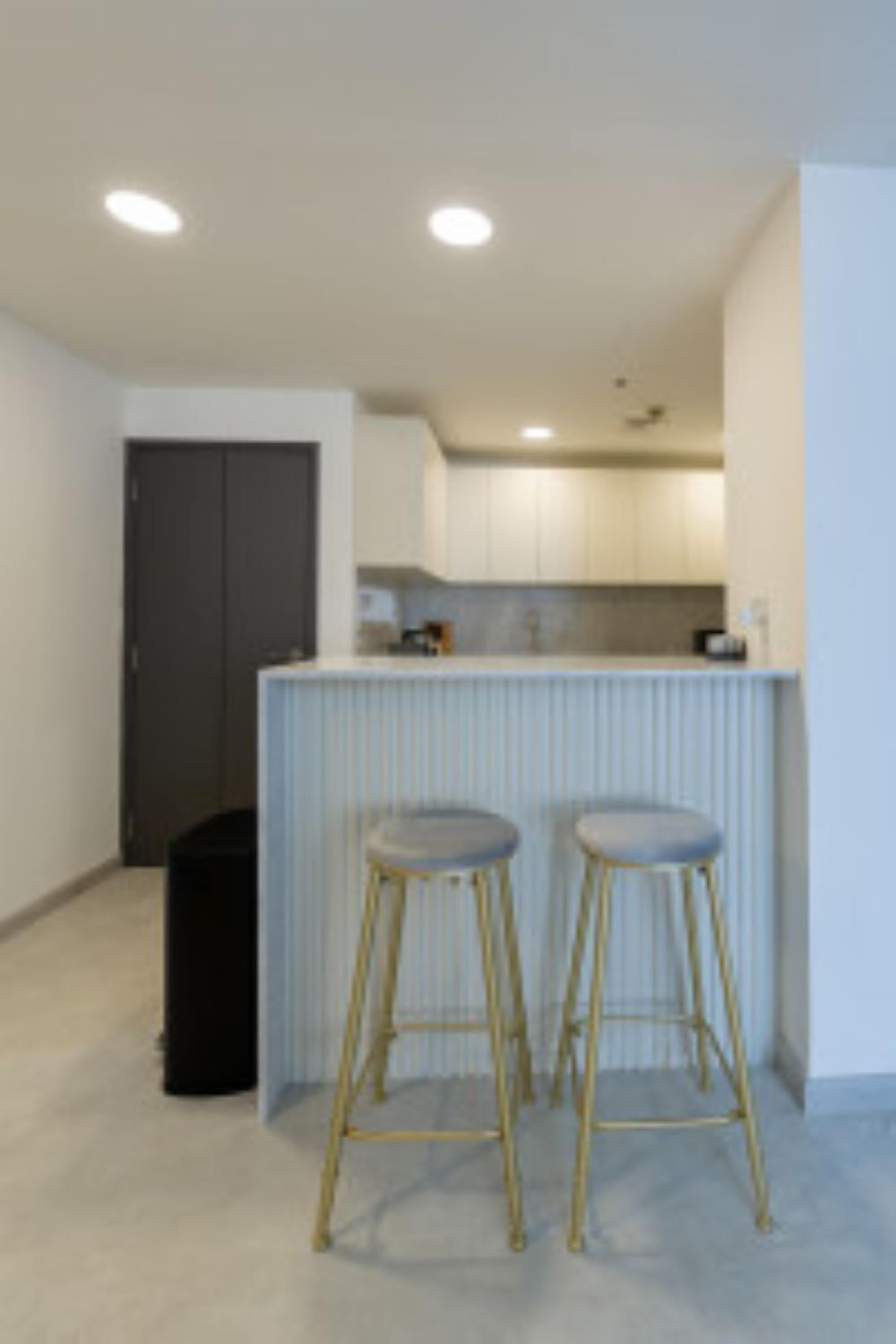 A modern kitchen with white cabinets, a countertop, and two stools.