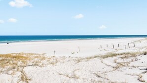 En bred sandstrand med klar himmel og rolig hav.