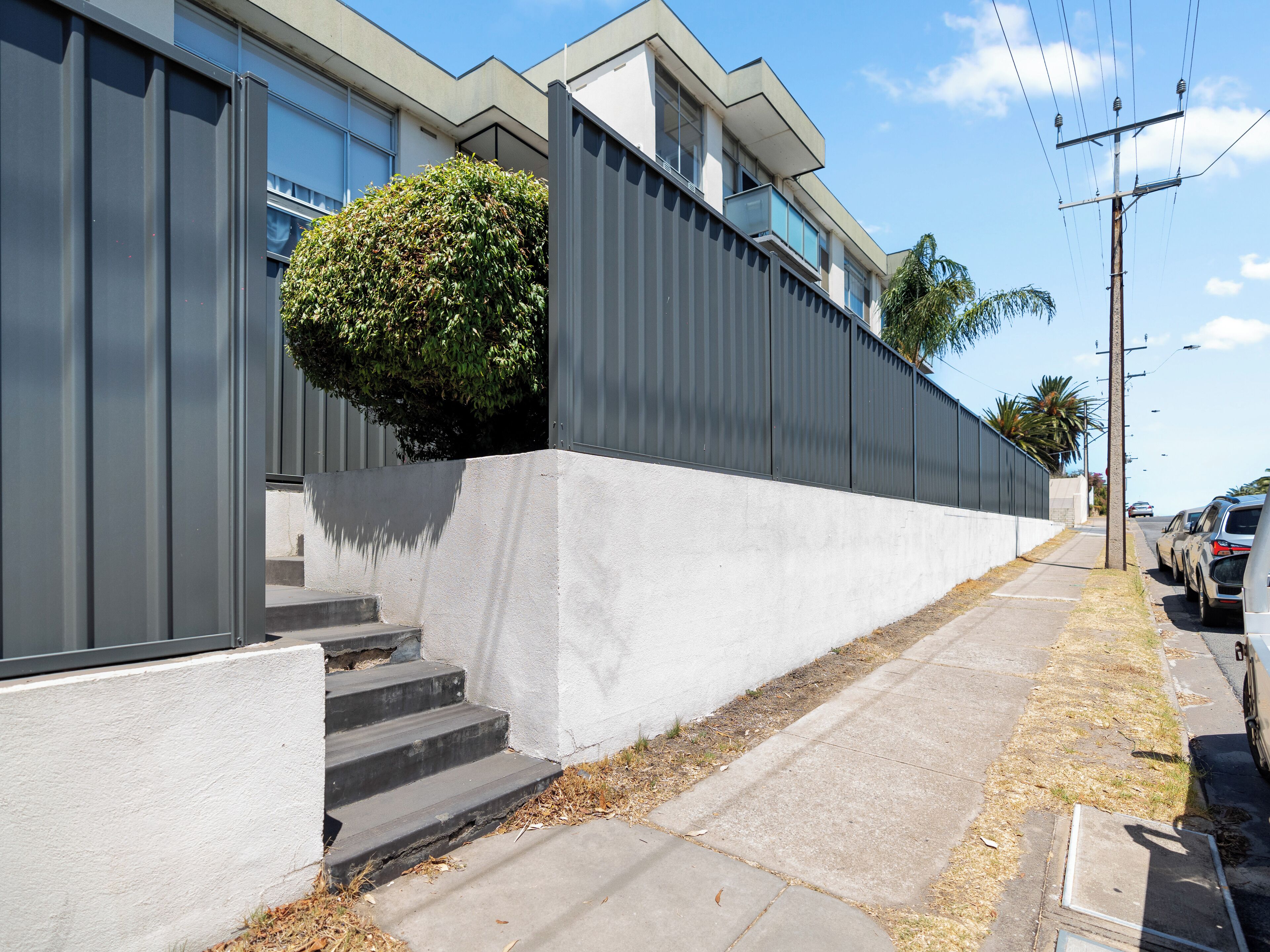 A modern building with a grey exterior, concrete steps leading to a white wall, and a small bush.