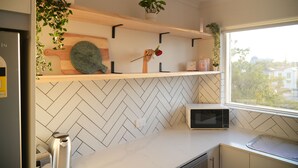 Una cucina con zellige a motivi a spina di pesce, mensole in legno con piante, un forno a microonde e un tostapane.