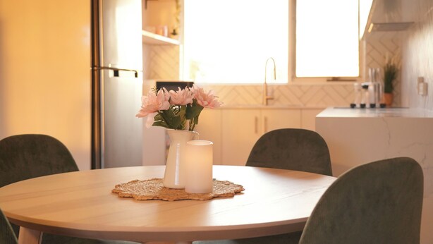 Una cucina moderna con un tavolo rotondo, sedie, un vaso di fiori e una candela.