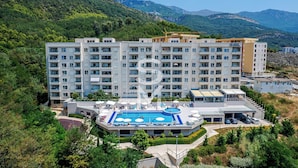 A multi-story hotel with a rooftop pool and a view of green hills. - Status apartments 173 (Becici)