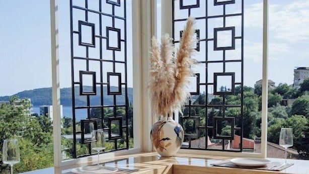 A dining area with a view of a mountainous landscape through a window with a geometric patterned screen. - Status apartments 173 (Becici)