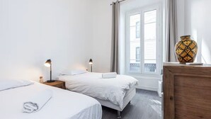 Une chambre d’hôtel avec deux lits, une commode en bois, un vase et une fenêtre avec des rideaux.