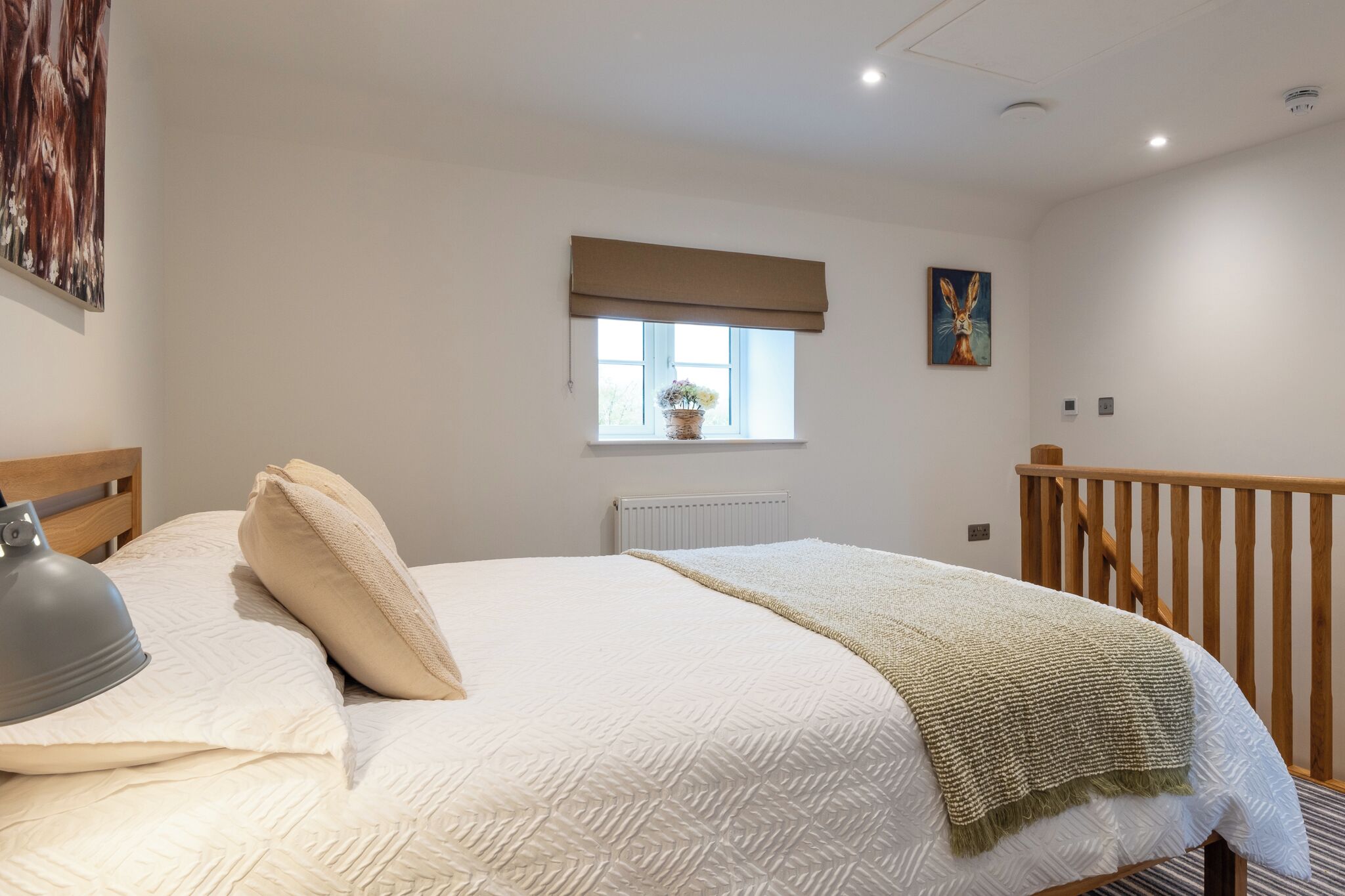 A bedroom with a bed, a window with a view, a radiator, and a wooden railing.