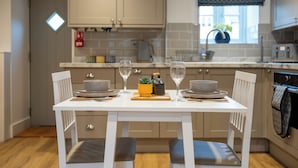 Une cuisine moderne avec des meubles blancs, une table à manger blanche dressée pour deux personnes et une fenêtre donnant sur l’extérieur.