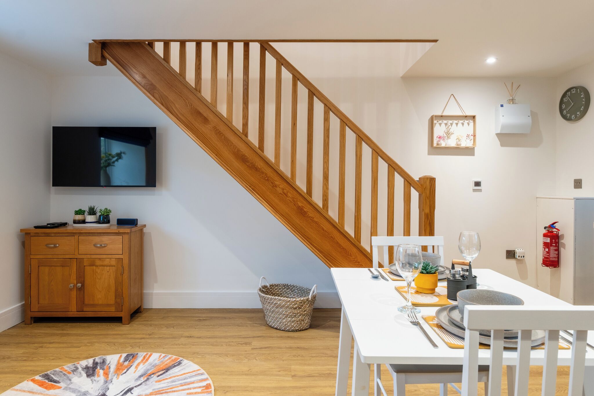Una cocina moderna con una escalera de madera, una mesa de comedor dispuesta con cristalería y un televisor montado en la pared.