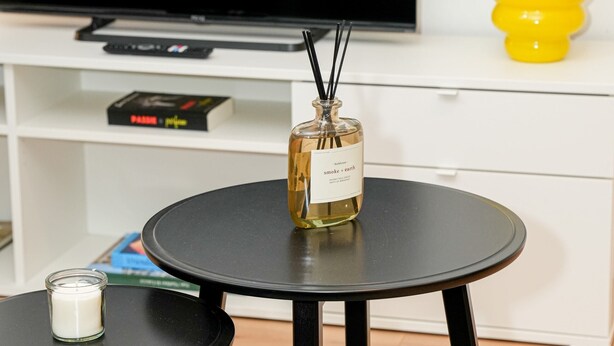 A modern living room with a flat-screen TV, a small round table with a candle, and a decorative vase on a white cabinet. - Modern 1BR 1LR Apartment Walk To Rabot (Ghent)