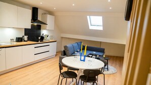 A modern kitchen with white cabinets, a black stove hood, and a round dining table with chairs. - Modern 1BR 1LR Apartment Walk To Rabot (Ghent)