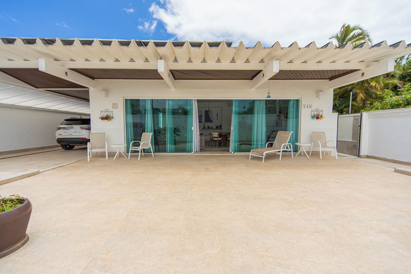 A covered outdoor area with a car parked nearby, a patio with chairs, and a glass door leading to an interior space.