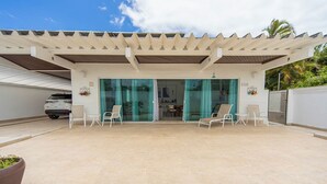 Un espacio al aire libre cubierto con un coche cerca, un patio con sillas y una puerta de cristal que da a un espacio interior.