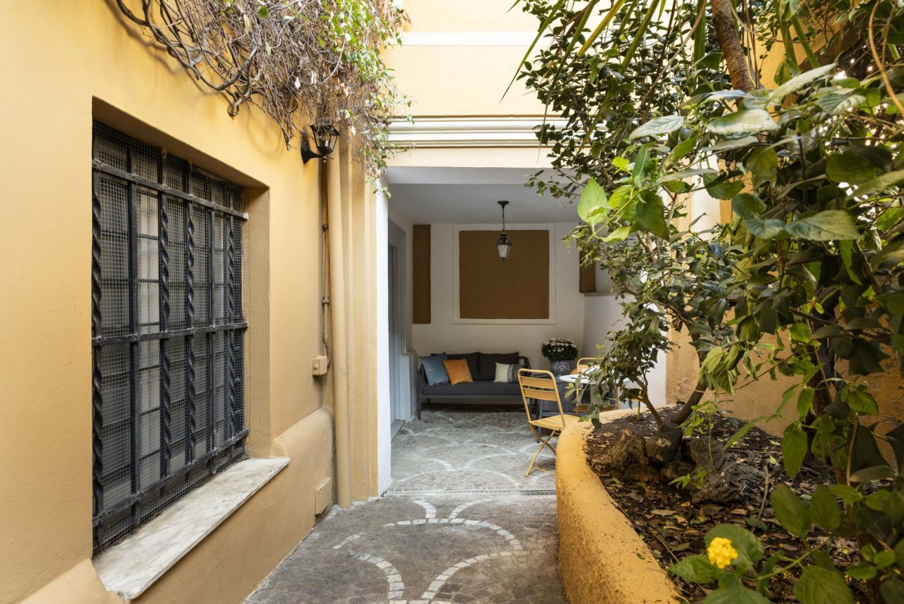 A narrow courtyard with a tiled floor, a window with metal bars, a sofa, and a chair.