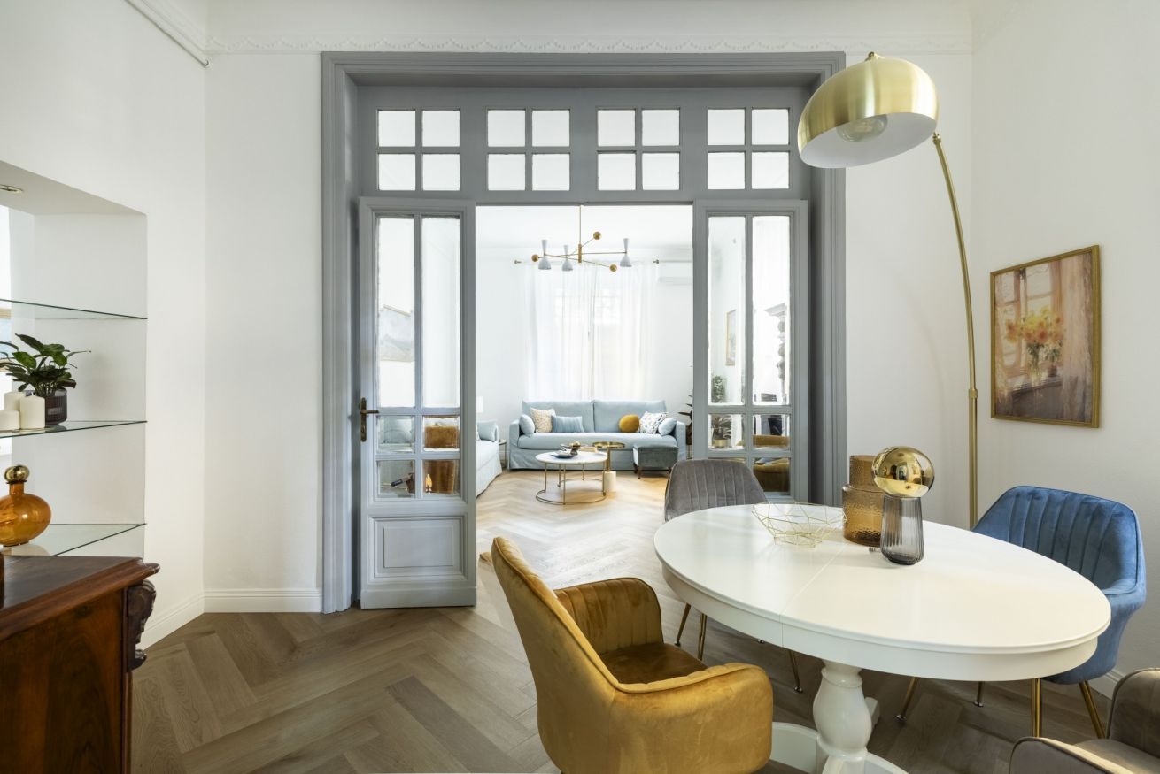 A dining area with a white table, gold chairs, and a gold pendant lamp.