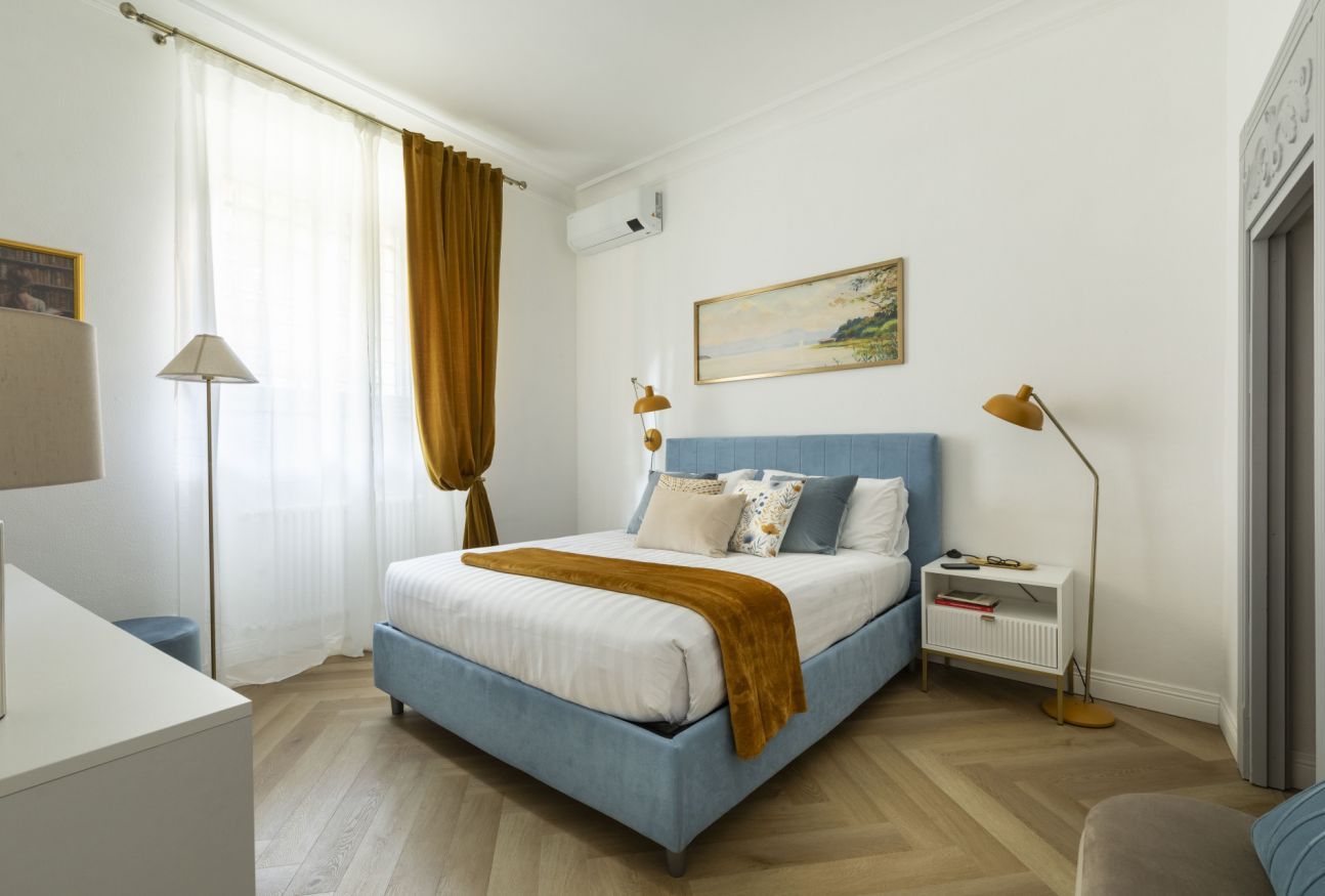 Een slaapkamer met een bed, nachtkastjes, een bureau en een schilderij aan de muur.
