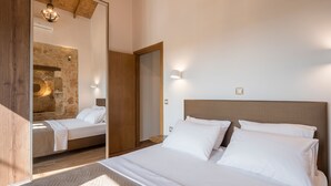 A bedroom with a large bed, a wooden headboard, a stone wall, and a mirror. - Stella s Traditional House Near the City (Chania)