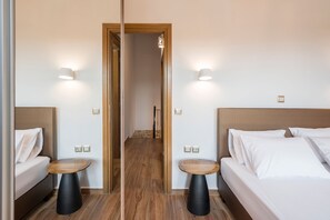 A hotel room with a mirrored wall, a wooden floor, two beds with white linens, and two round tables. - Stella s Traditional House Near the City (Chania)