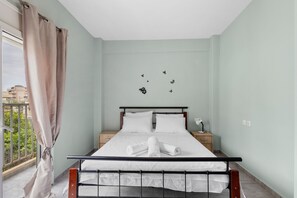 A neatly made bed with white linens and a rolled towel, a bedside table with a lamp, and a view of the outside balcony. - Litsa s Maisonette Near Sea - City Center (Chania)