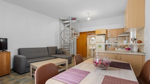 A modern living room with a grey sofa, a wooden dining table, and a spiral staircase leading to the kitchen. - Litsa s Maisonette Near Sea - City Center (Chania)