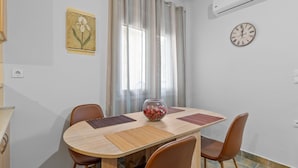 A dining area with a wooden table, four chairs, a decorative bowl, a clock, and a window with curtains. - Litsa s Maisonette Near Sea - City Center (Chania)