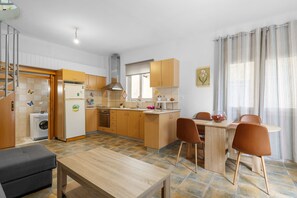 A modern kitchen with wooden cabinets, a dining table with chairs, a washing machine, and a refrigerator. - Litsa s Maisonette Near Sea - City Center (Chania)