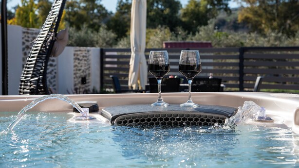 Un bain à remous avec deux verres de vin rouge, entouré d’une clôture en bois et d’arbres.
