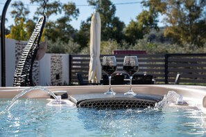 Un bain à remous avec deux verres de vin rouge, entouré d’une clôture en bois et d’arbres.