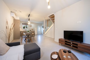 Una sala de estar moderna con televisor de pantalla plana, un sofá, un comedor y una escalera.