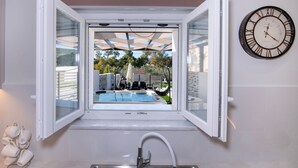 Une cuisine avec une fenêtre donnant sur une piscine, un évier en acier inoxydable et une horloge murale.