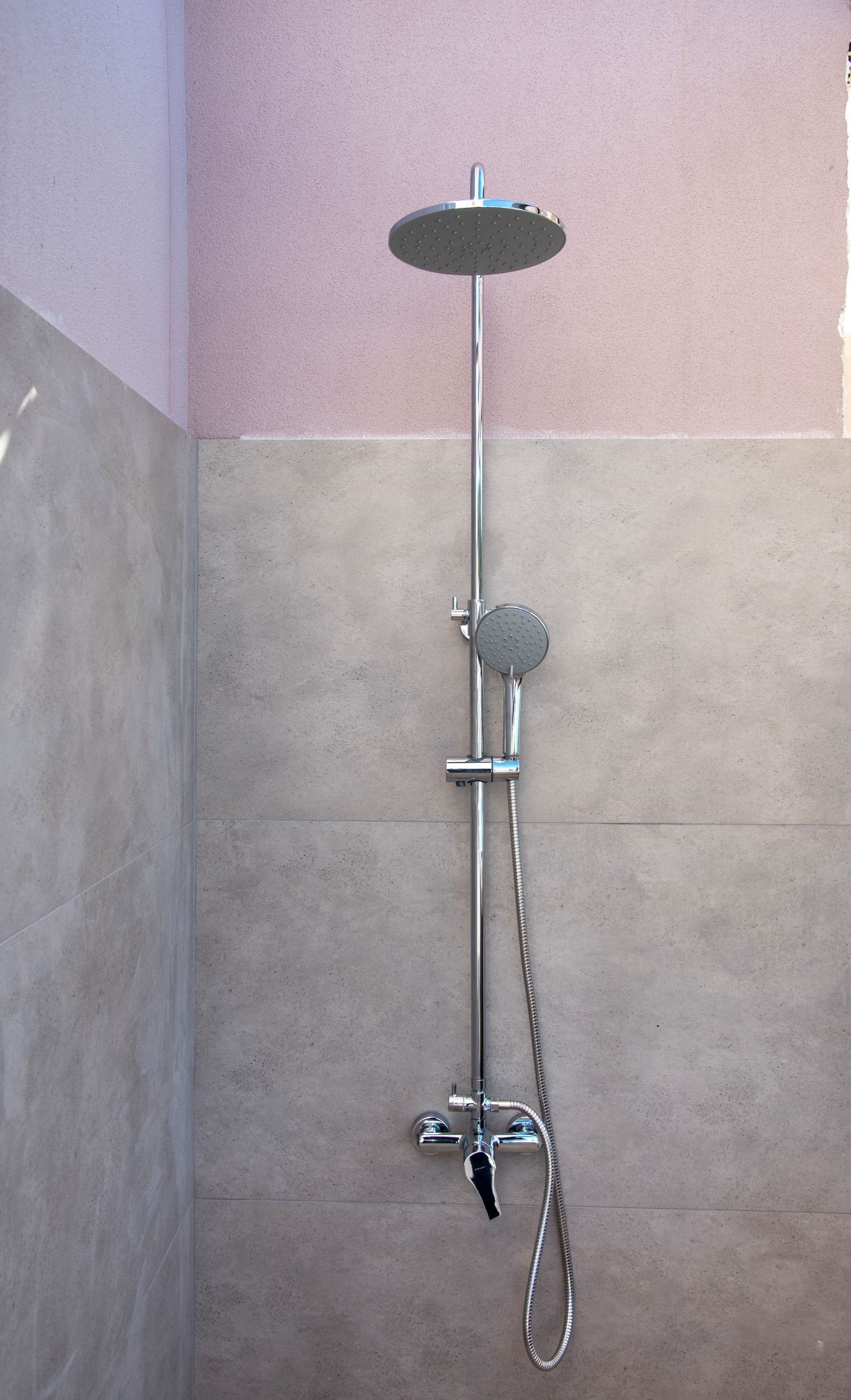 Ducha con cabezal de ducha de mano y un cabezal de ducha fijo en el techo, instalada en una pared con suelo de baldosas.