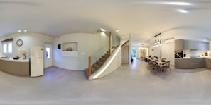 Una cocina moderna con una isla curva, electrodomésticos integrados y una escalera que lleva a un comedor.