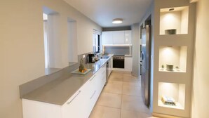 Une cuisine moderne avec des meubles blancs, un grand îlot central et des étagères intégrées.