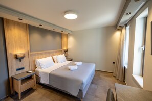 Habitación de hotel moderna con una cama grande, mesitas de noche, un escritorio y una ventana con cortinas.