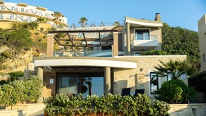 A modern two-story building with a balcony, stone facade, and surrounding greenery. - Villy Luxury Home by the Sea 2 (Chania)