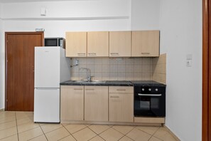 Eine Küche mit hellen Holzschränken, einem weißen Kühlschrank, einem schwarzen Herd und einer gefliesten Spritzwand.