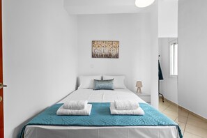 Ett modernt hotellrum med en stor säng, vita sängkläder, en turkosfärgad pläd och en tavla på väggen.