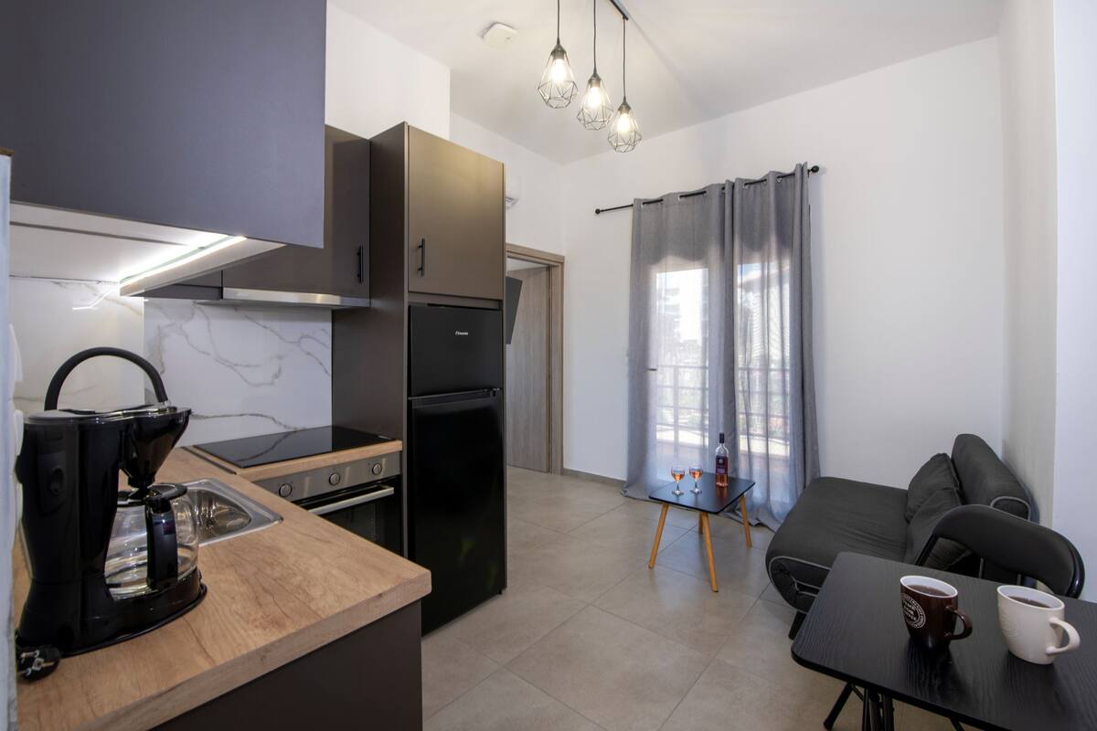 A compact kitchen with a coffee maker, a refrigerator, and a dining area with a table and chairs.