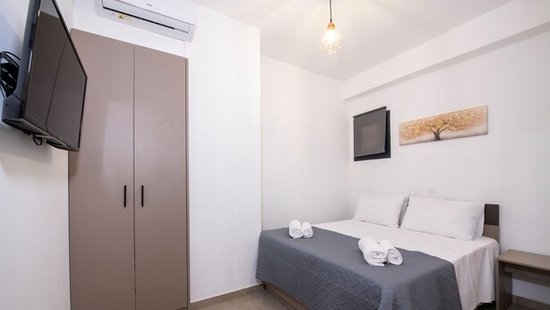 A hotel room with a bed, a wardrobe, a flat-screen TV, and a painting on the wall. - Halepa Apartment's in Chania (Chania)