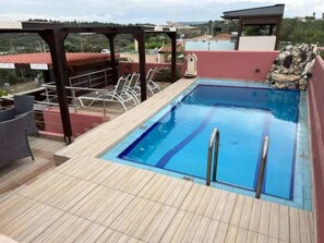 A rectangular swimming pool with a wooden deck, surrounded by lounge chairs and a pergola. - Villa Smaro With Private Pool (Chania)