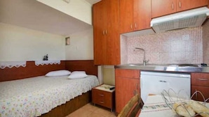 A small, compact room with a single bed, a wooden cabinet, a tiled backsplash, and a built-in dishwasher. - Villa Smaro With Private Pool (Chania)