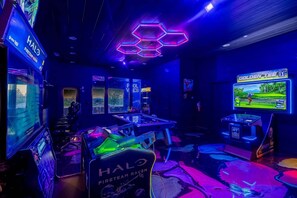 A gaming room with multiple gaming stations, neon signage, and a large screen displaying a game.