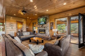 A cozy log cabin interior with a stone fireplace, leather sofas, and a dining area.