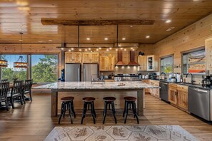 A modern kitchen with wooden cabinets, a large island with stools, stainless steel appliances, and pendant lighting.